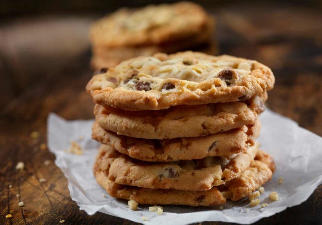 gourmet chocolate chip cookies stacked on a napkin on top of wood table